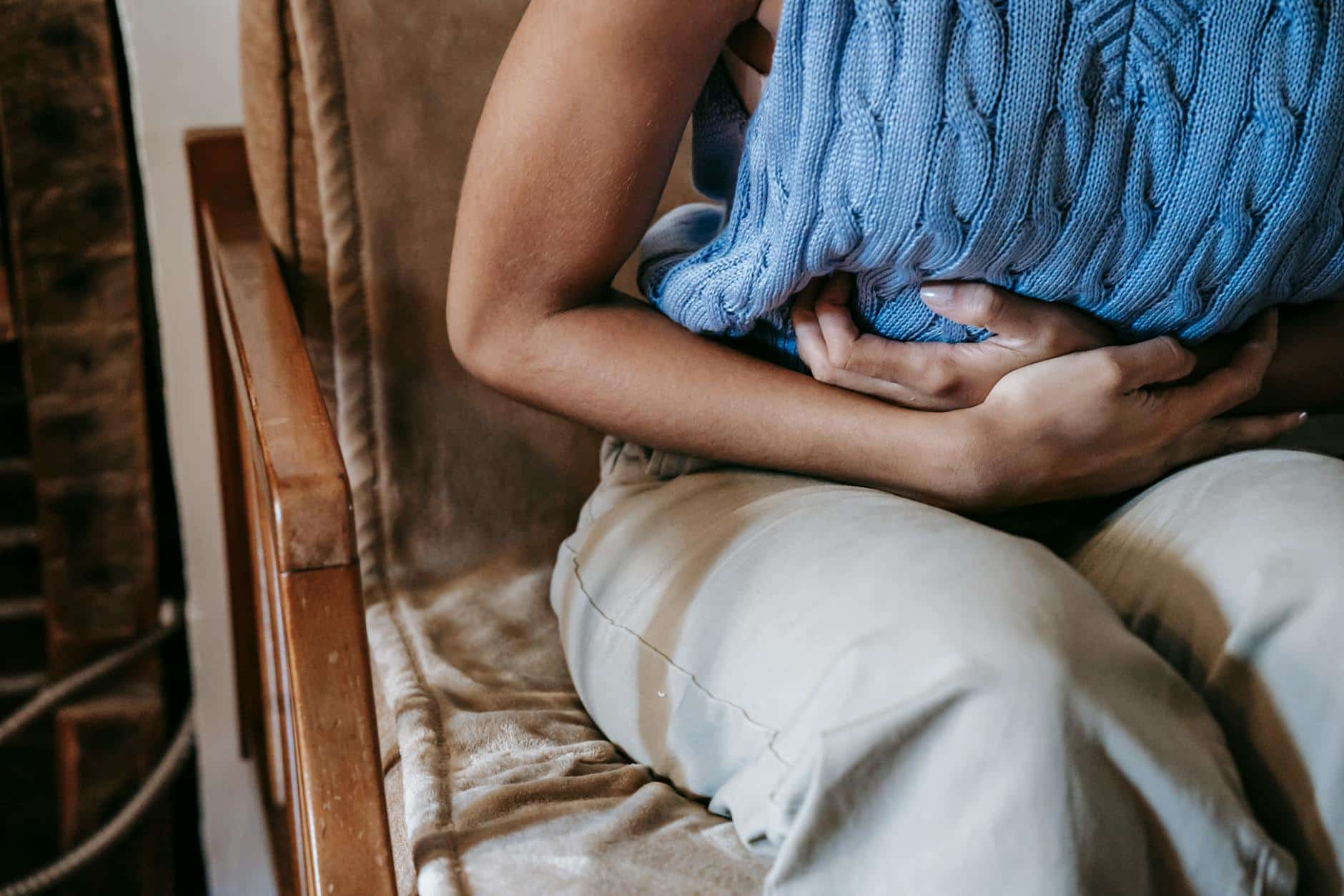 Femme allongée sur canapé avec bouillotte sur le ventre, douleur menstruelle
