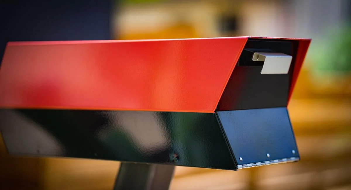 Close-up of a modern red and black mailbox outdoors with a blurred background.